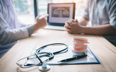 A dental patient consulting with their dentist while both sides sit at a desk